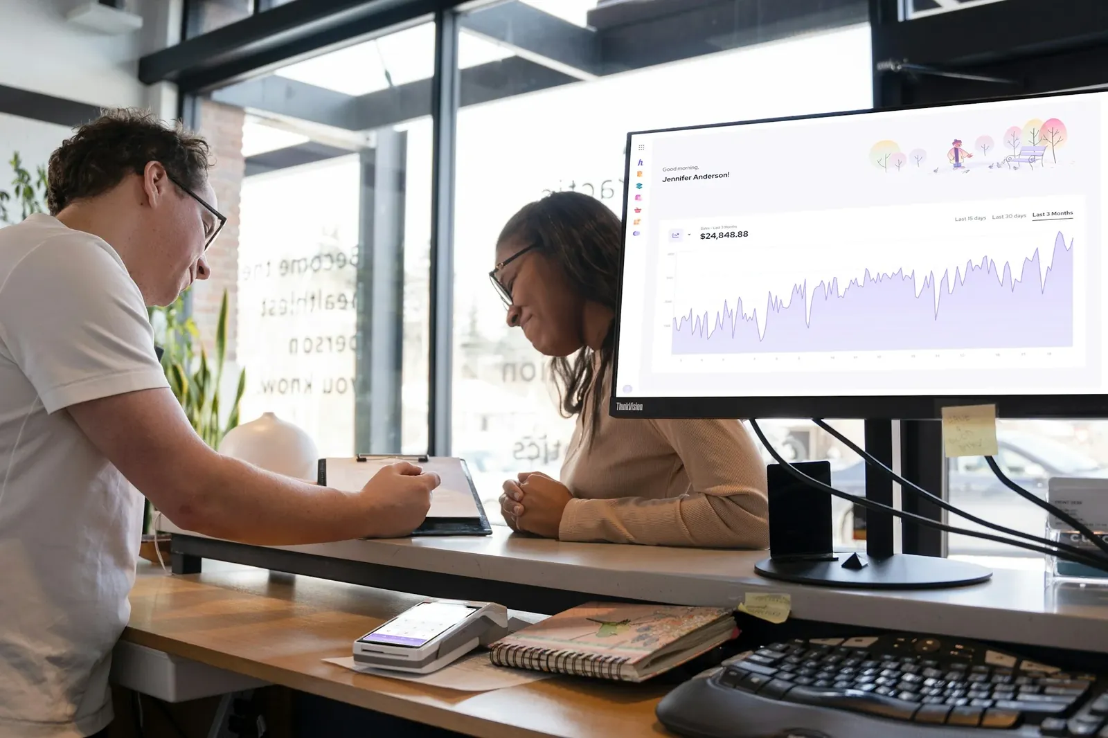Colleagues at standing desks with a dashboard on screen