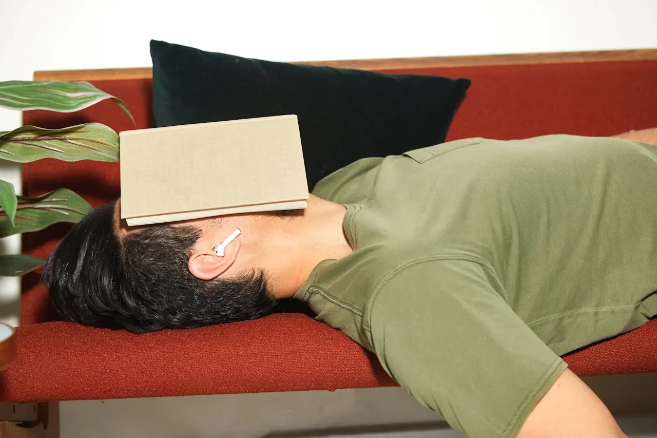 Man lying on a red sofa with a book over his face