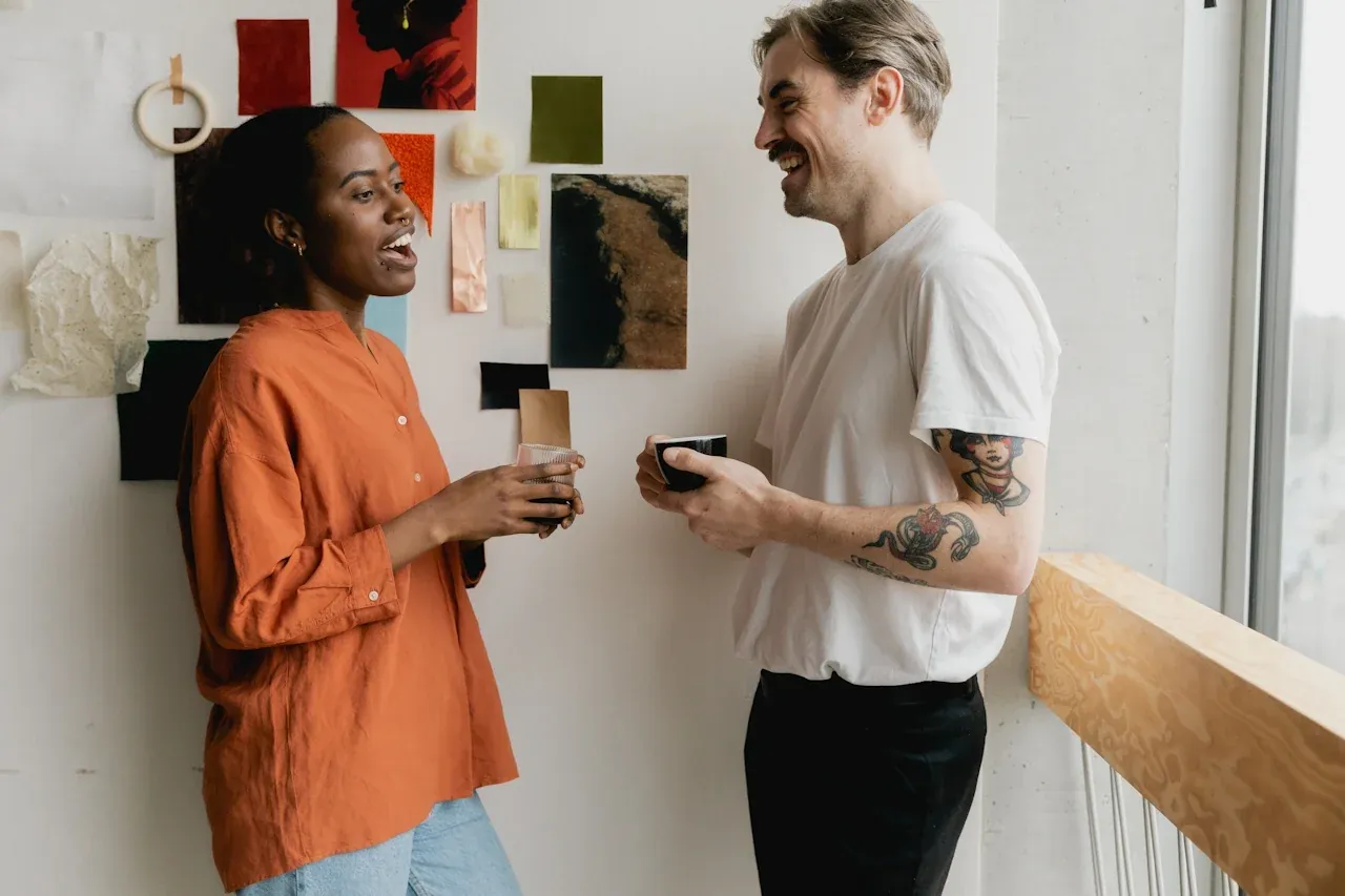 Two colleagues chatting over coffee by a pinboard